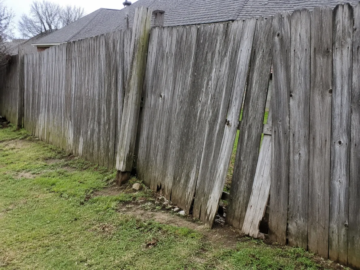 Old weathered gray privacy fence with warped, split boards and a leaning post, ready for wood fence installation near me Tulsa, OK