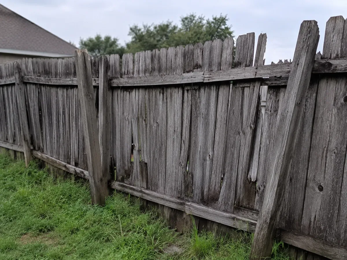 Old residential wood fence leaning and weathered gray with rotted, gapped boards, ready for a residential fence company near me Tulsa, OK