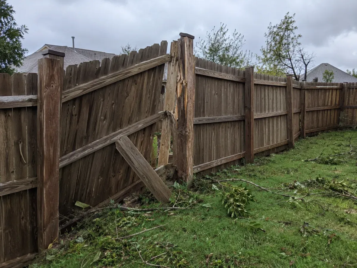 Storm-damaged wood fence leaning after high wind with a cracked post, time for fence repair near me Tulsa, OK